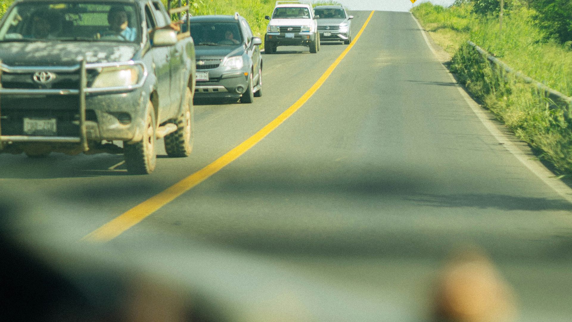 a group of cars driving down a road next to a lush green field