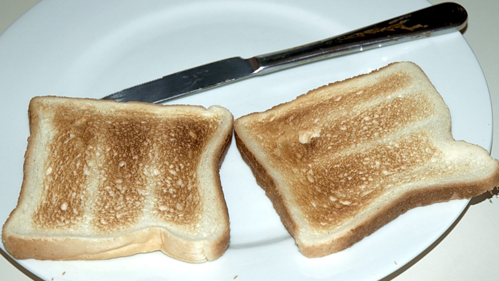 Two pieces of Toast on a plate with a knife.