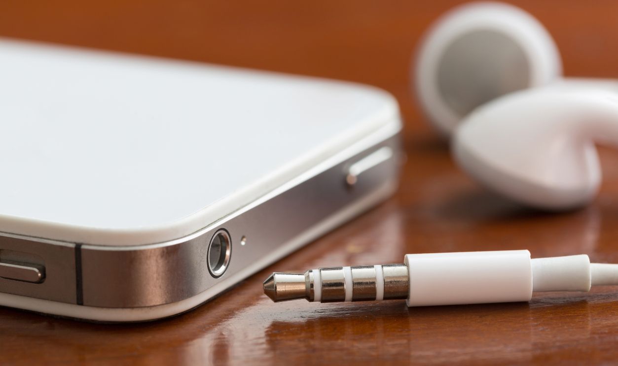 Close-up of a smartphone, earbuds, jack and port on a table with shallow depth of field