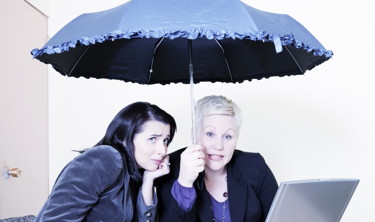 Shutterstock - 208286713 - Two businesswomen under an umbrella indoors.