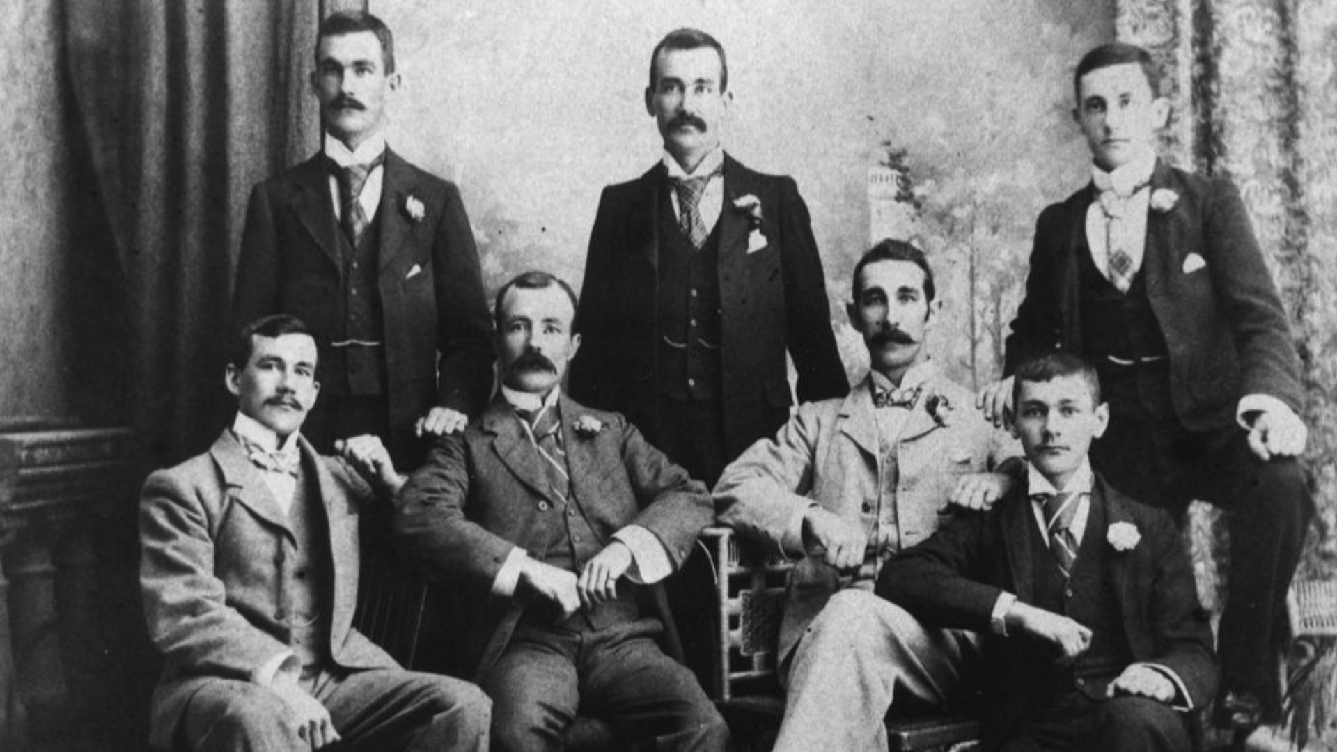 Group of men wearing three-piece suits, posing for a portrait, 1890-1900
Seven men, all wearing single-breasted, three-piece suits, posing for a group portrait in the 1890s.