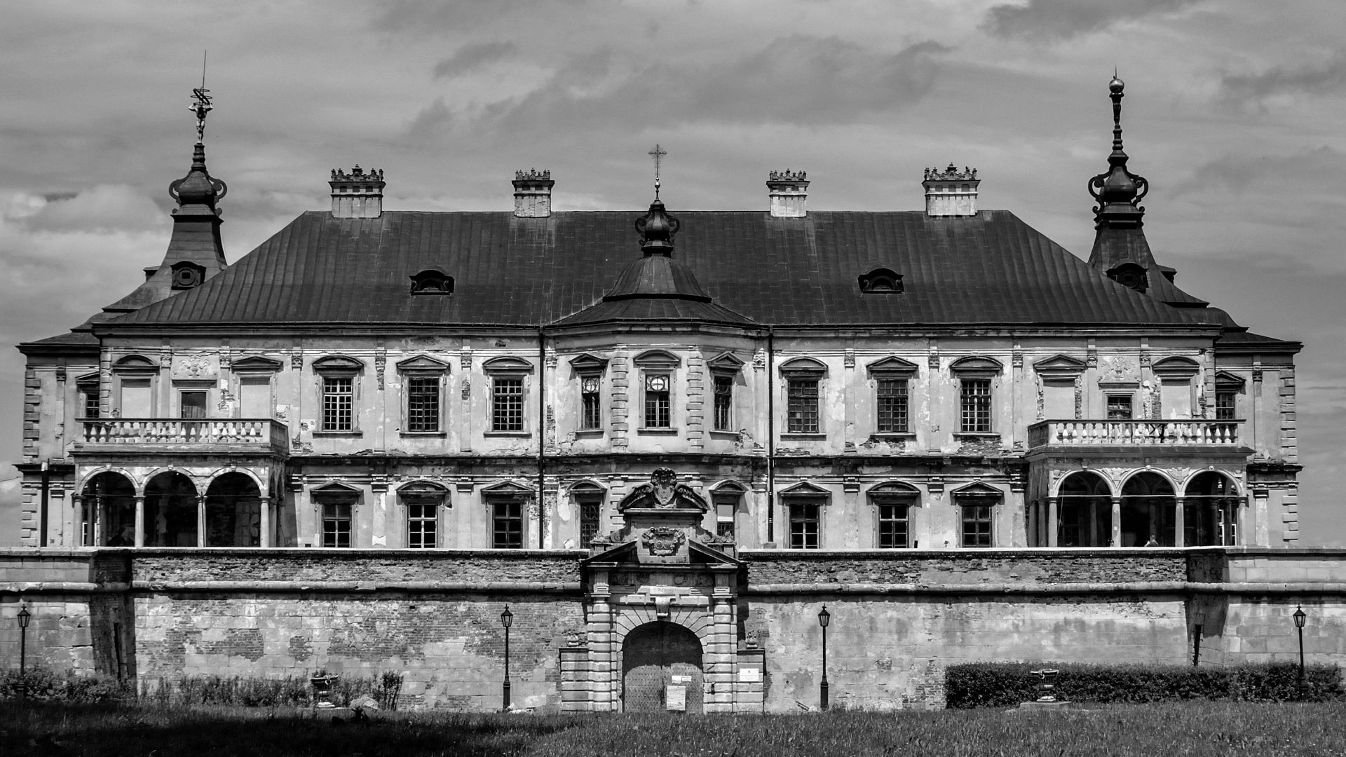 Black and white of aged building exterior near masonry fence under cloudy sky in Ukraine