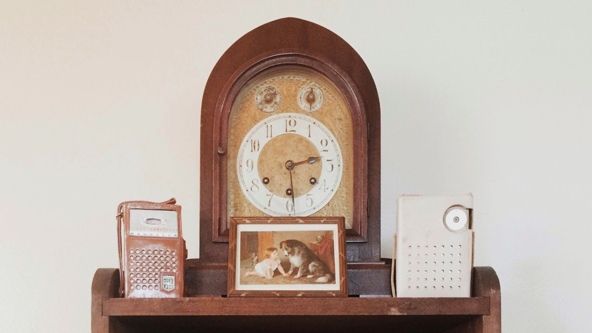 A collection of vintage radios and a globe on a wooden shelf with an antique clock.
