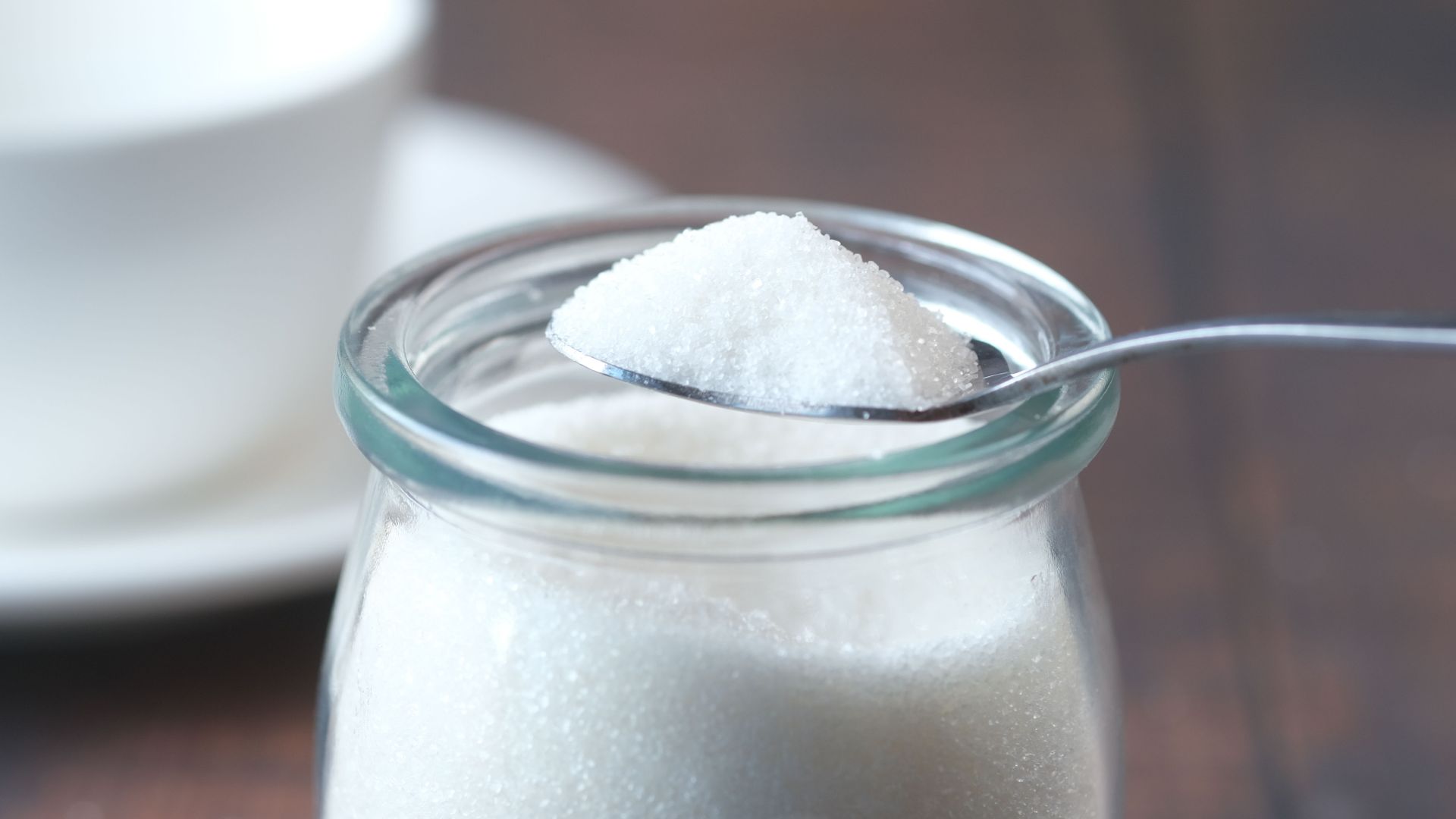 A close-up shot of white sugar in a glass jar, delicately scooped with a spoon. Ideal for food concepts.