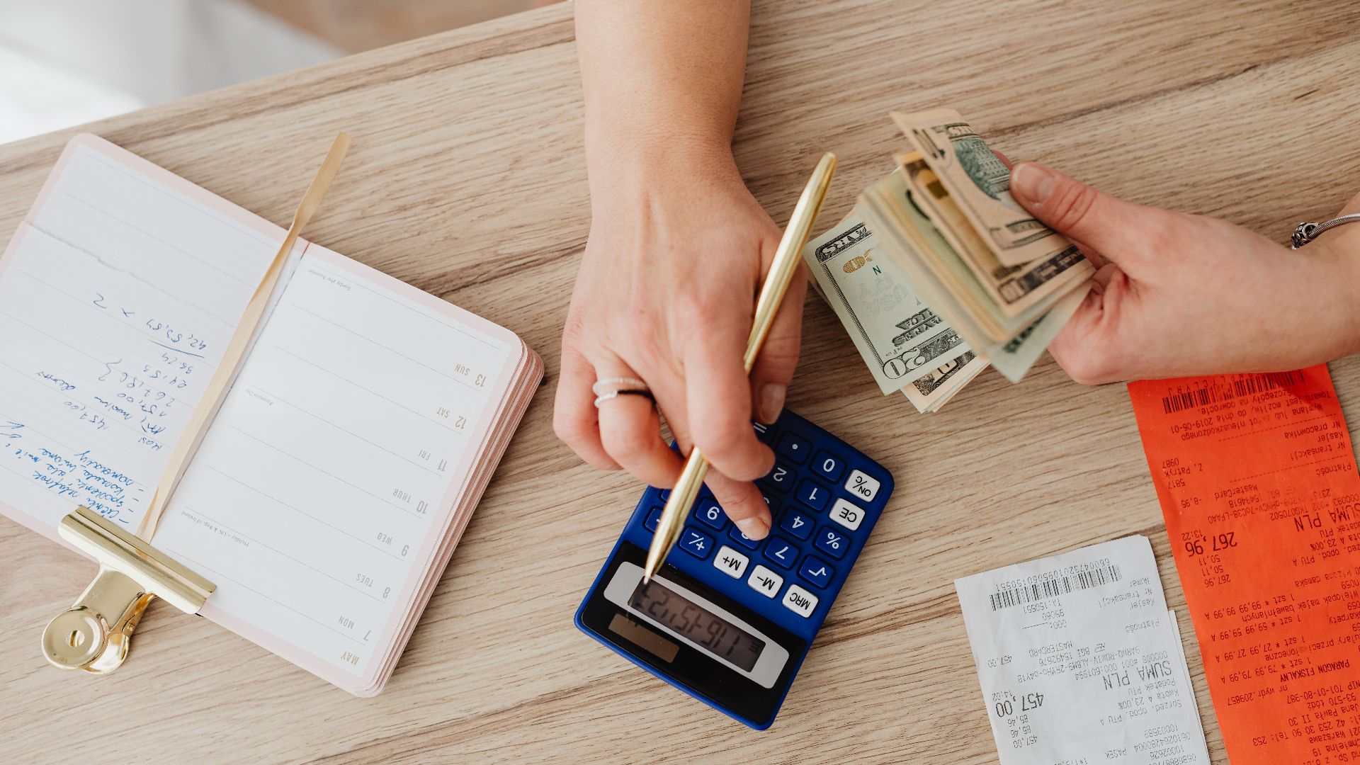 Hands managing finances with calculator, cash, and receipts on a wooden table. Ideal for budgeting concepts.