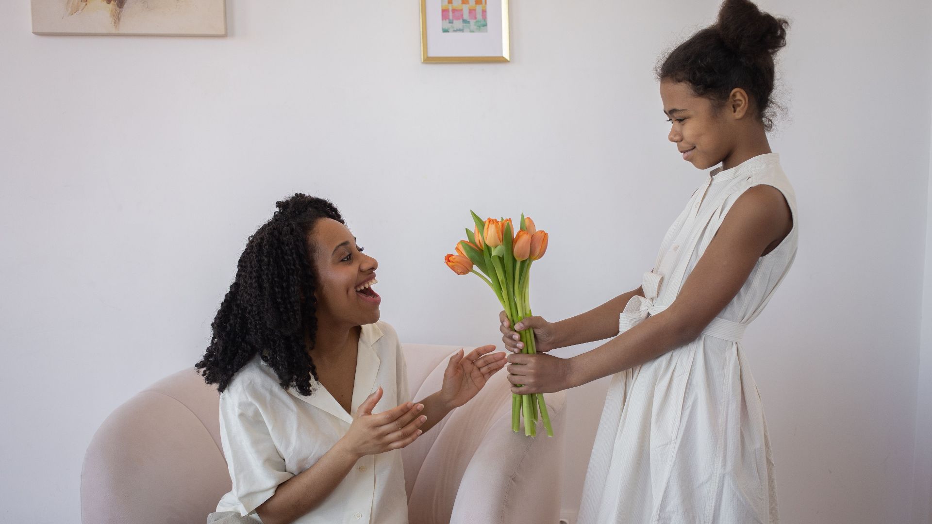 A daughter surprises her mother with a bouquet of tulips at home, capturing love and happiness.