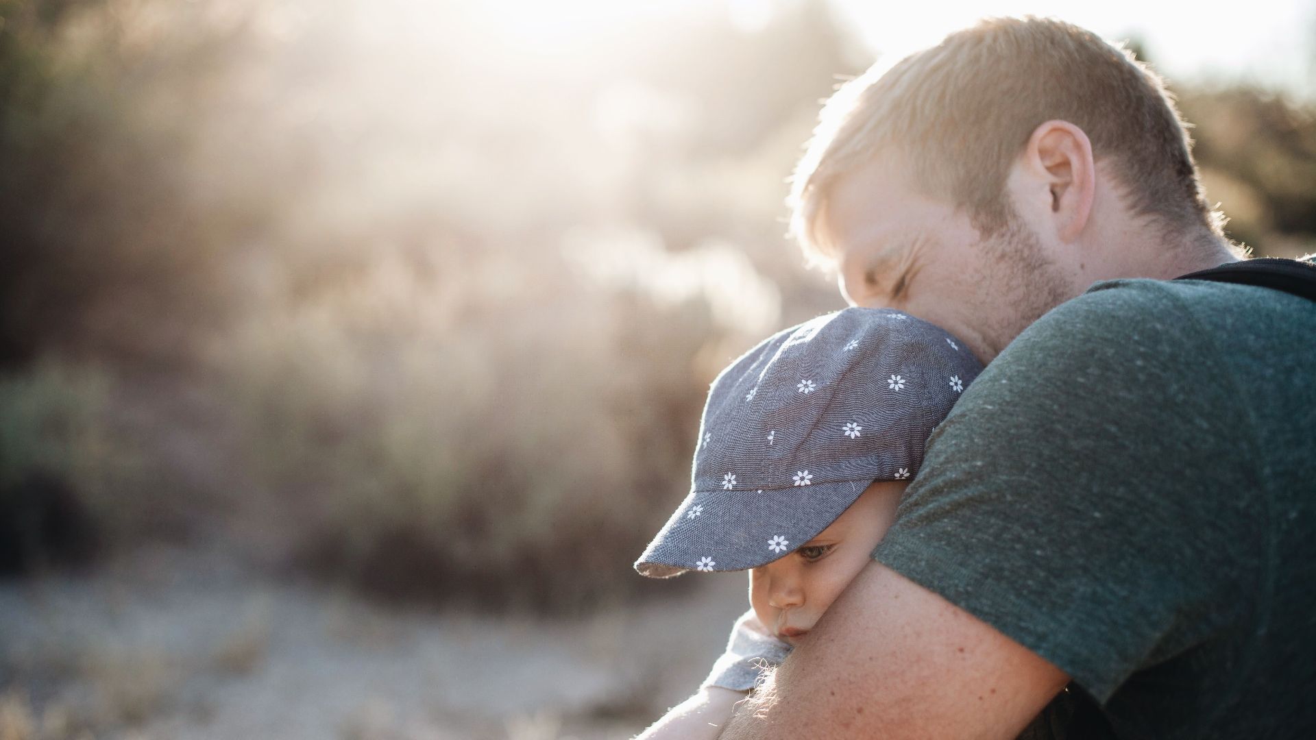 A father lovingly embraces his baby outdoors on a sunny day. Perfect for Father's Day themes.