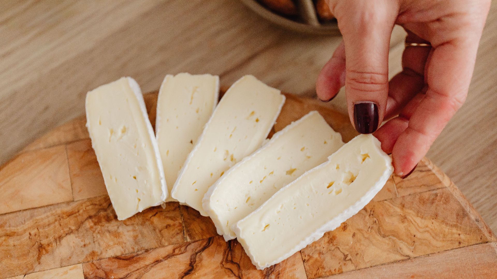 Hand holding fresh creamy brie cheese slices on wooden board, perfect for gourmet dishes.