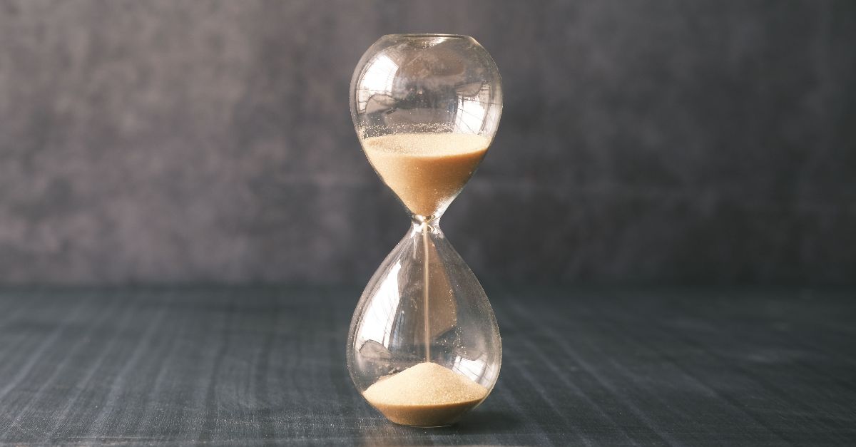A close-up of a classic hourglass with sand slowly passing through, set against a textured background.