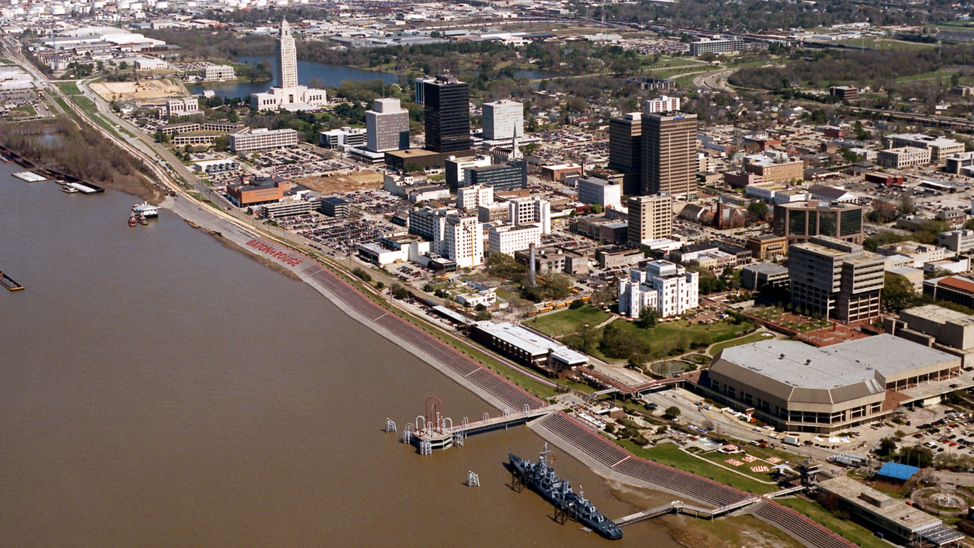 Aerial view of the riverfront area of Baton Rouge, Louisiana, USA. The city fronts on the Mississippi River in the center of Louisiana. The tall state capitol tower can be seen at center left. The historic destroyer USS Kidd is moored in the river at the 