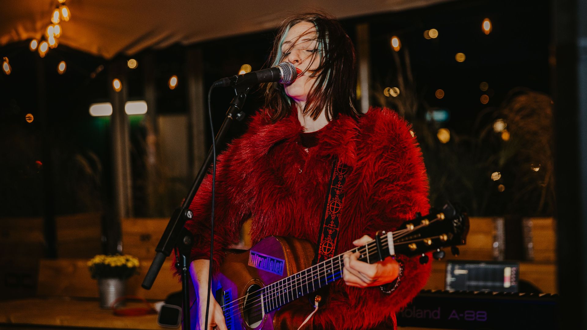 Vibrant live music performance with female singer playing guitar on stage under string lights.