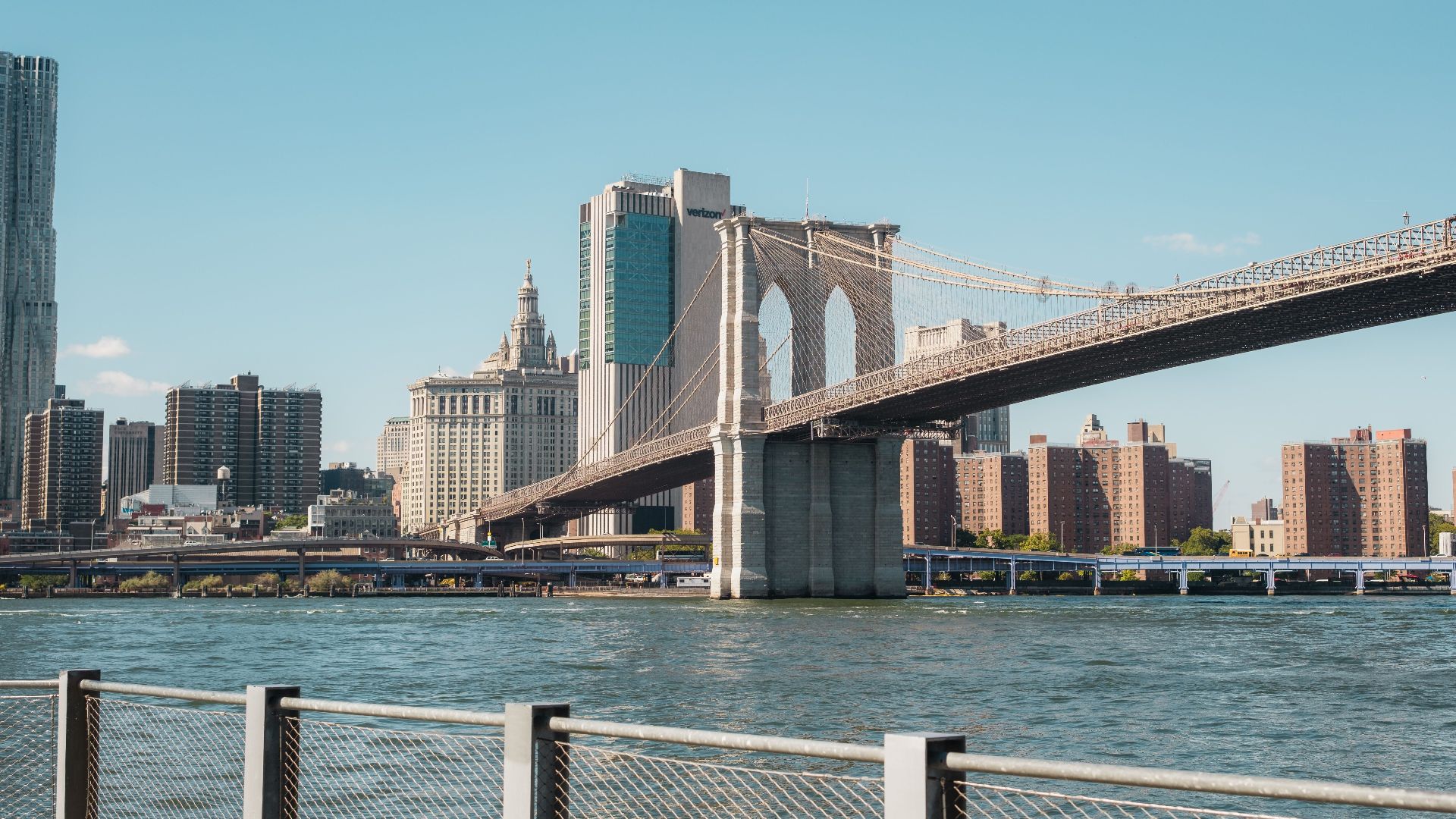 View of the Brooklyn Bridge and Manhattan skyline under a clear sky.