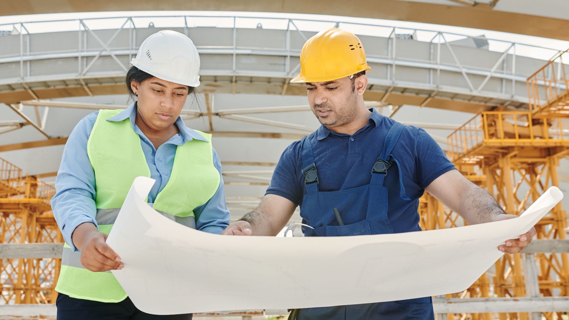 Male and female engineers discussing blueprints at a construction site, promoting teamwork and planning.