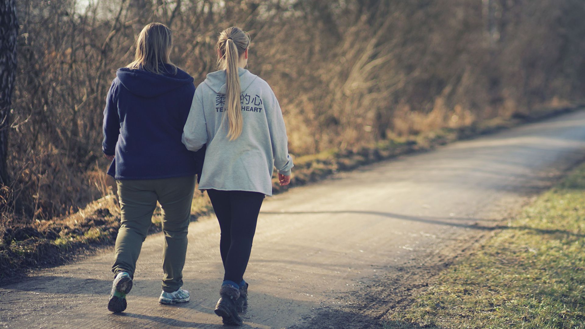 Two women enjoy a peaceful walk on a park path, surrounded by spring foliage.