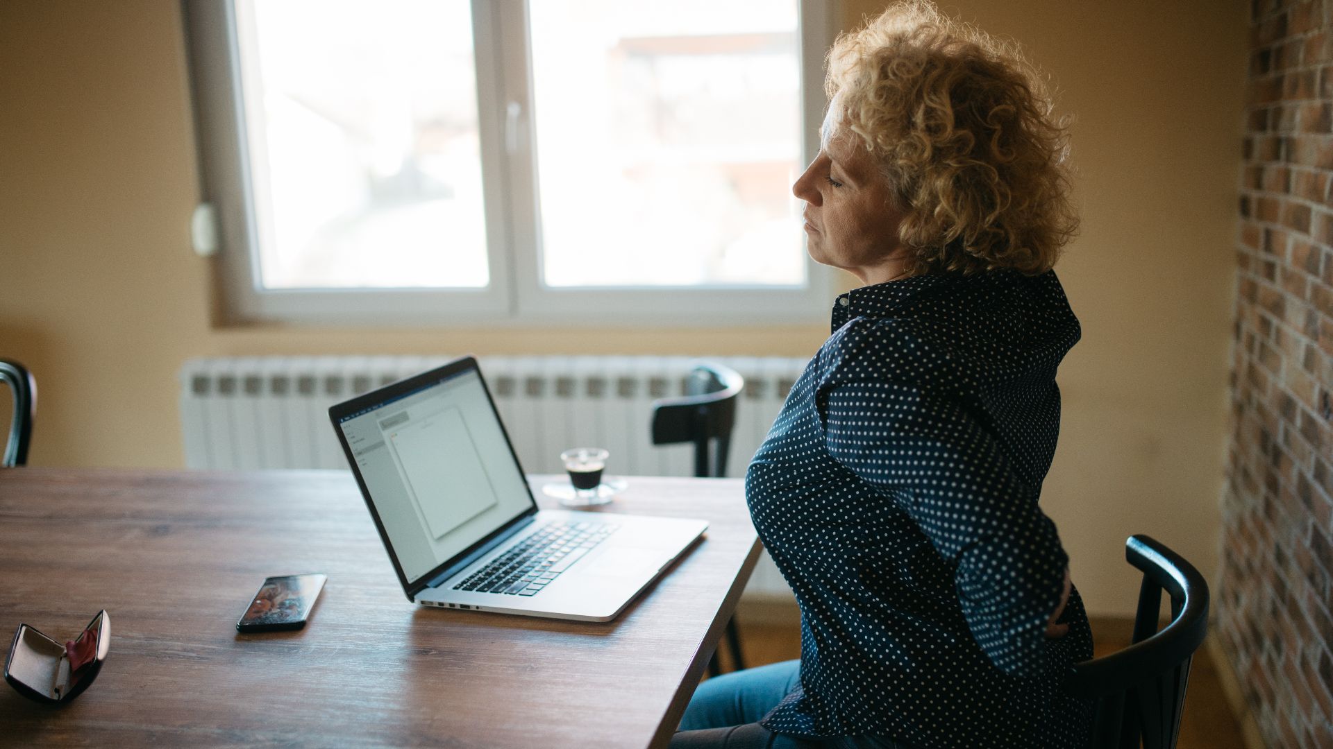 Middle-aged woman with curly hair working on a laptop and having back spine pain