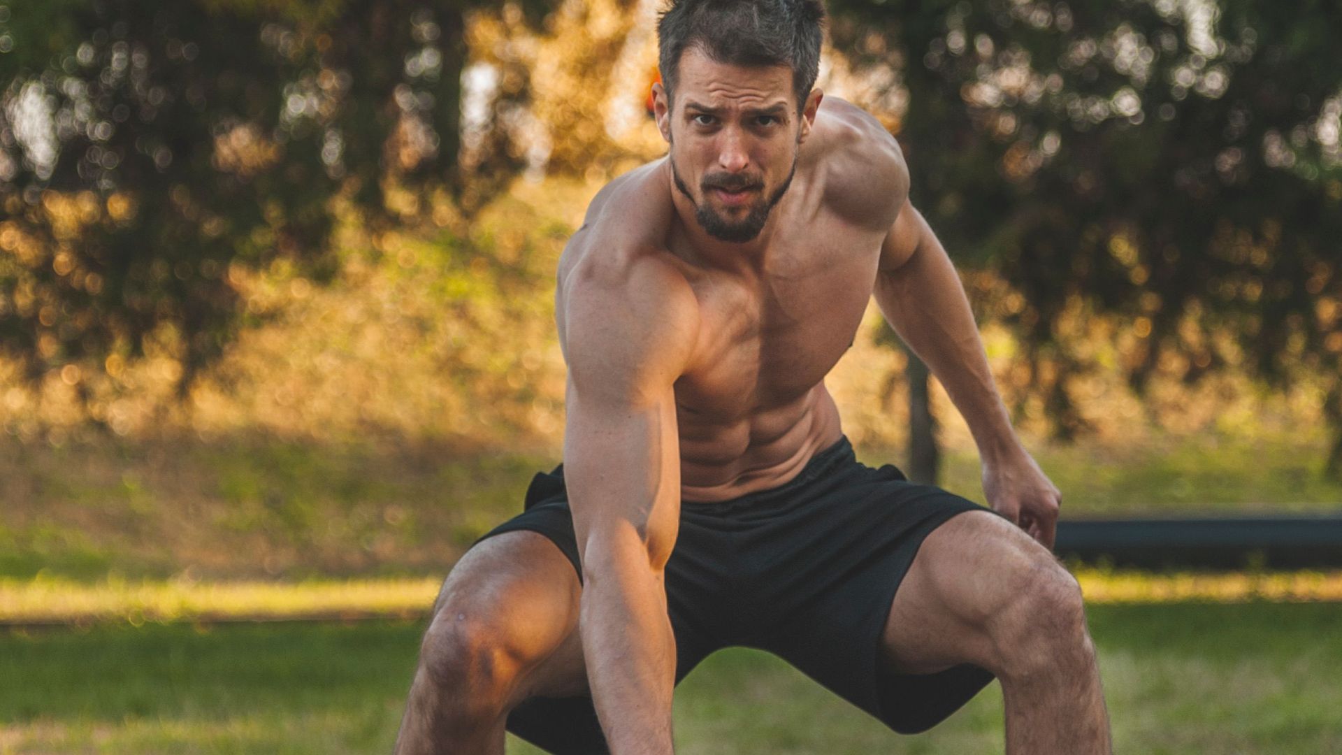 A muscular man exercises with tires in a park during fall.
