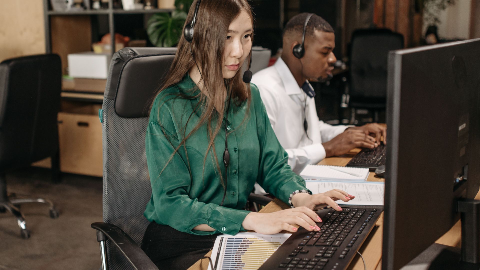 Colleagues using computers and headsets in a modern office setting emphasizing teamwork and productivity.
