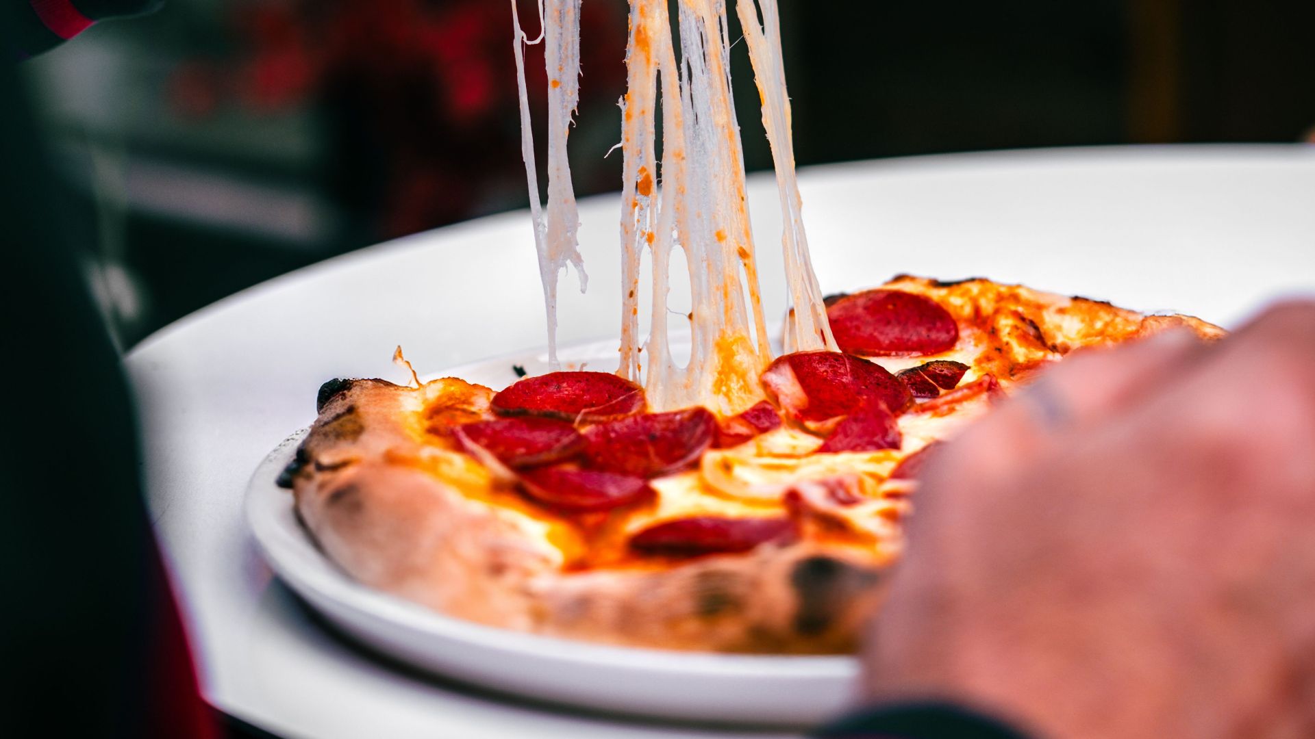 Close-up of a hand holding a pepperoni pizza slice with a gooey cheese pull, creating an appetizing scene.