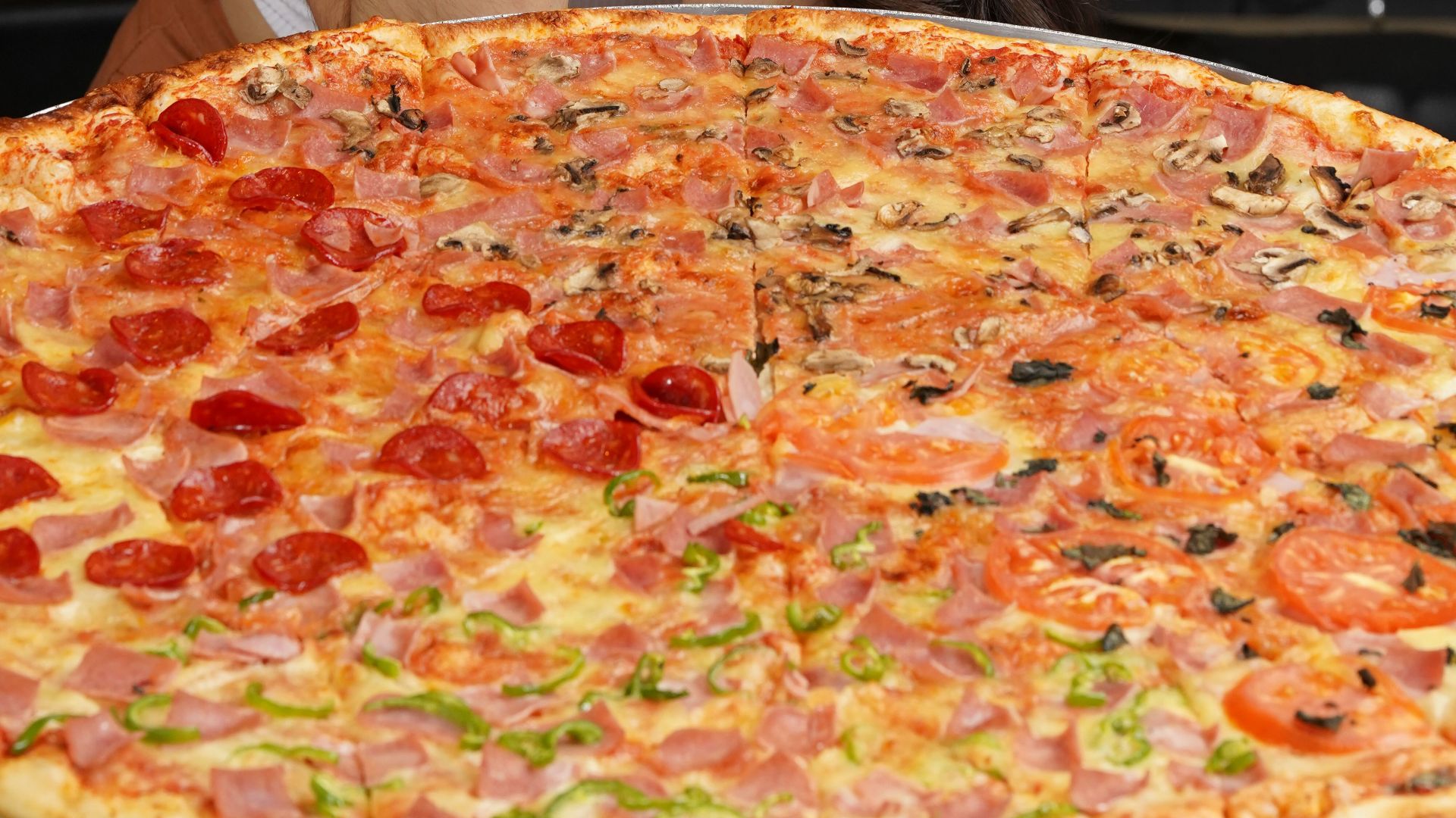 A woman eagerly anticipates enjoying a large, delicious pizza with multiple toppings indoors.
