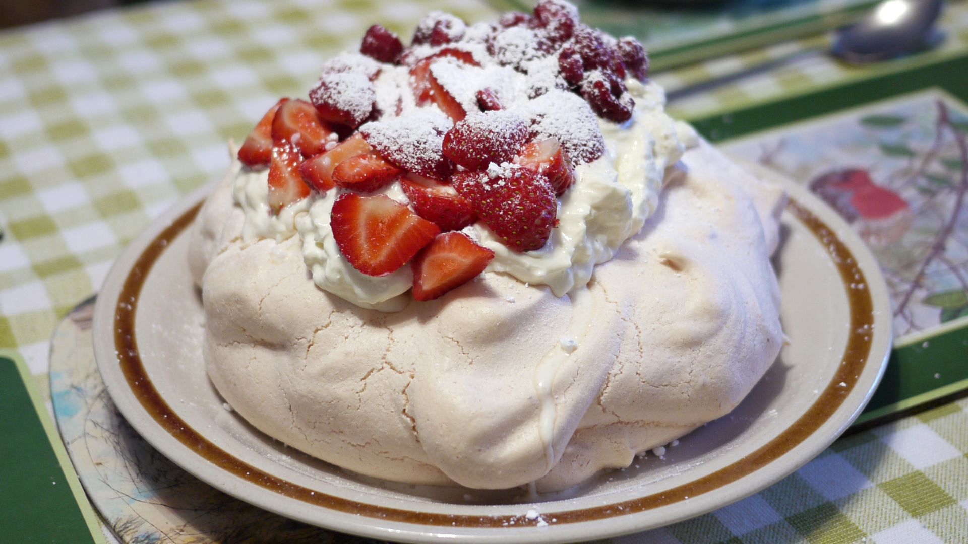 Pavlova garnished with cream and strawberries.