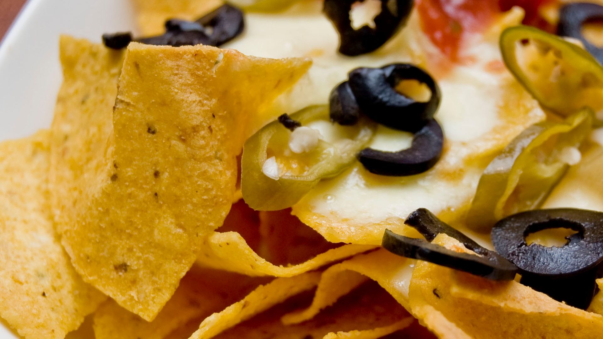 A plate of Nachos—tortilla chips topped with melted cheese, sliced chile peppers, sliced black olives, and chili sauce—as served by the Logenhaus Roast & Grill in the UEP Subang Jaya township of Selangor, Malaysia.Cheese Nachos