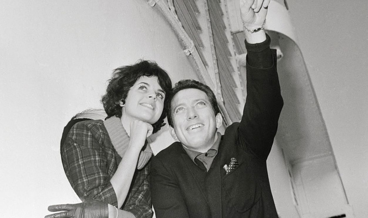 Singer Andy Williams points while standing with fiancee Claudine Longet, who is looking out from a porthole.