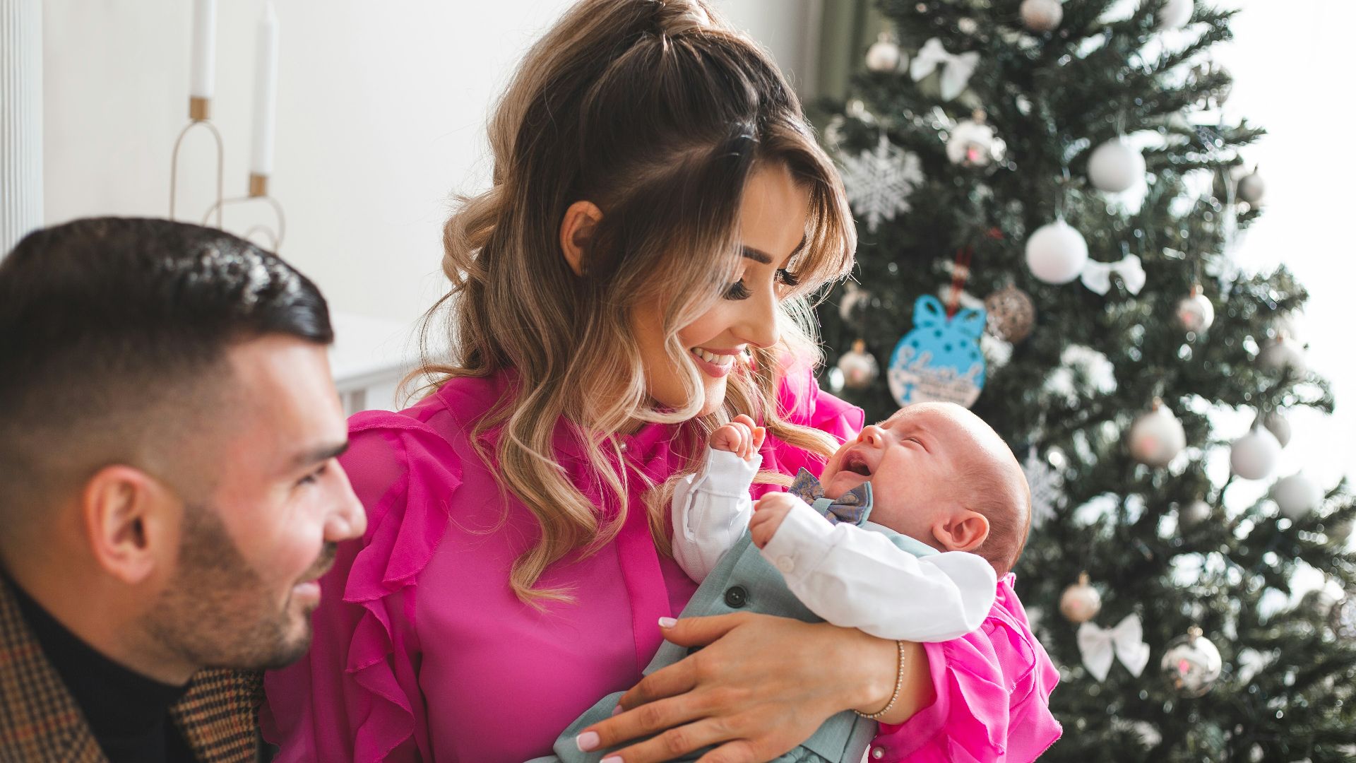 Parents holding their newborn baby near christmas tree