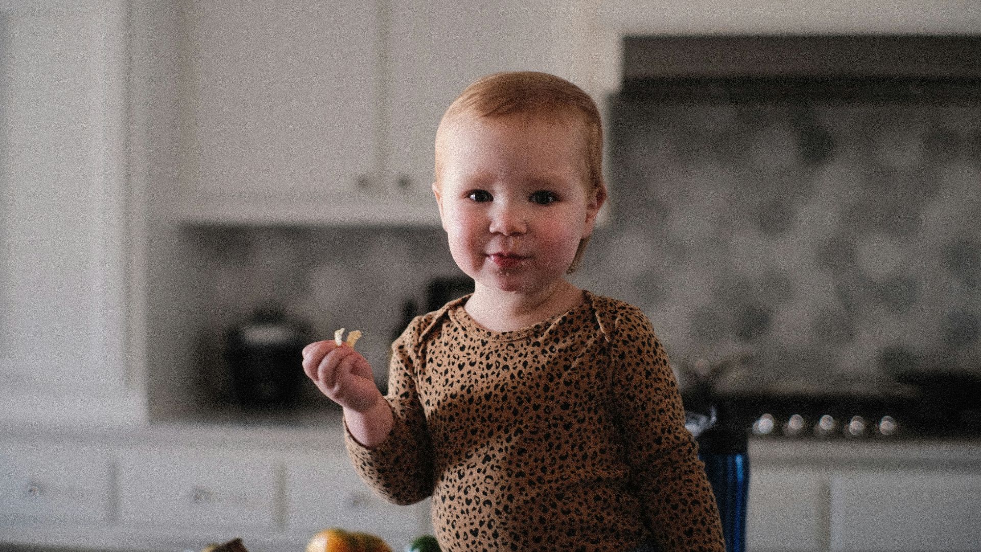 a little girl standing in a kitchen holding a piece of food