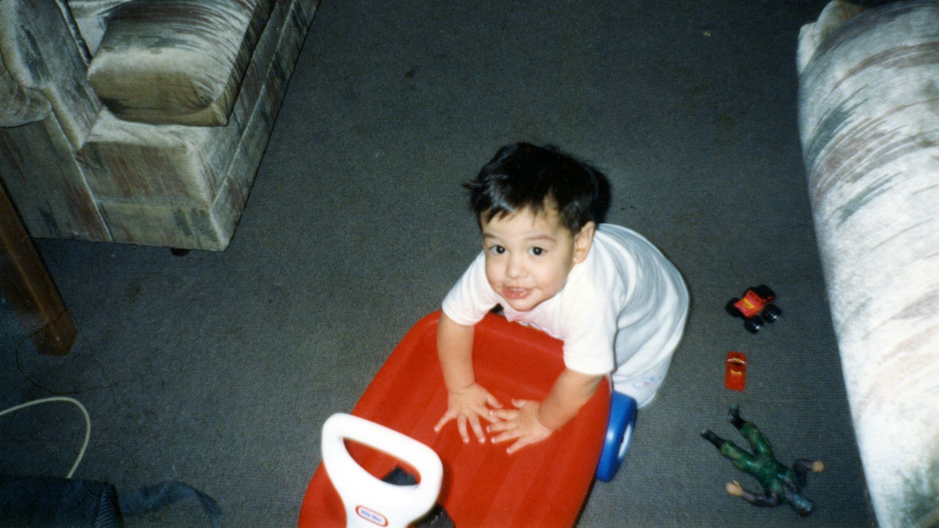 A smiling baby on a red toy looking up
