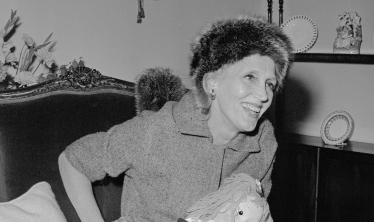 American author Kay Thompson (1909 - 1998) seated in an armchair and holding a doll, September 30th 1958.