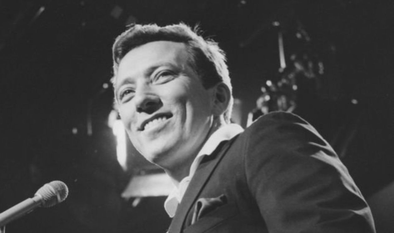 Andy Williams, US singer, sits smiling beside a microphone in a publicity still issued for his television show, 'The Andy Williams Show', USA, 1966.