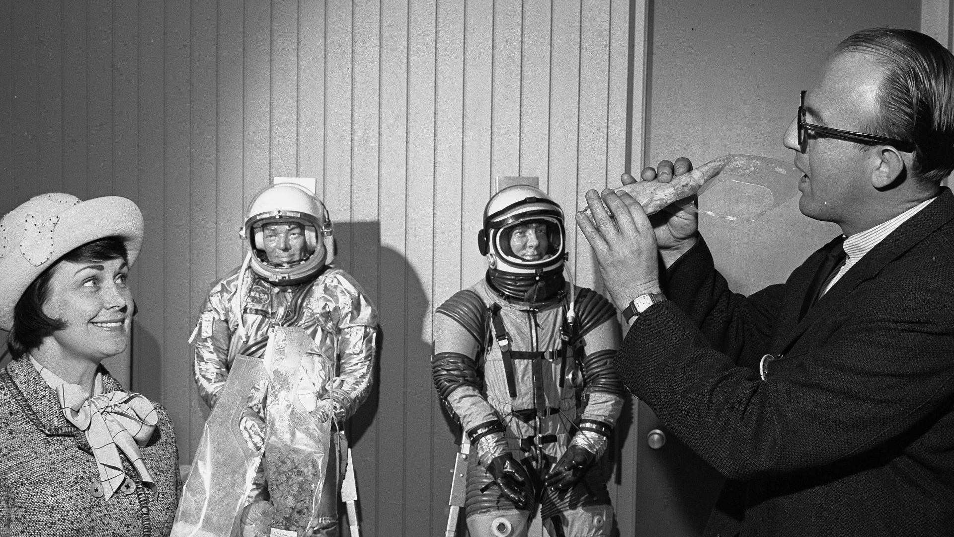 Frank J. Roberts, Apollo engineer demonstrating how astronauts eat to ARCS treasurer, Marion DeFore, Calif., 1965