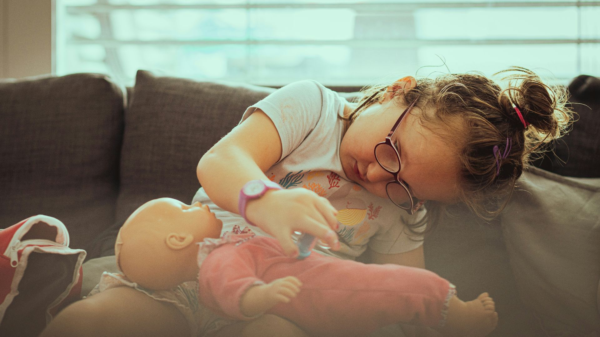 A little girl is playing with a doll on the couch