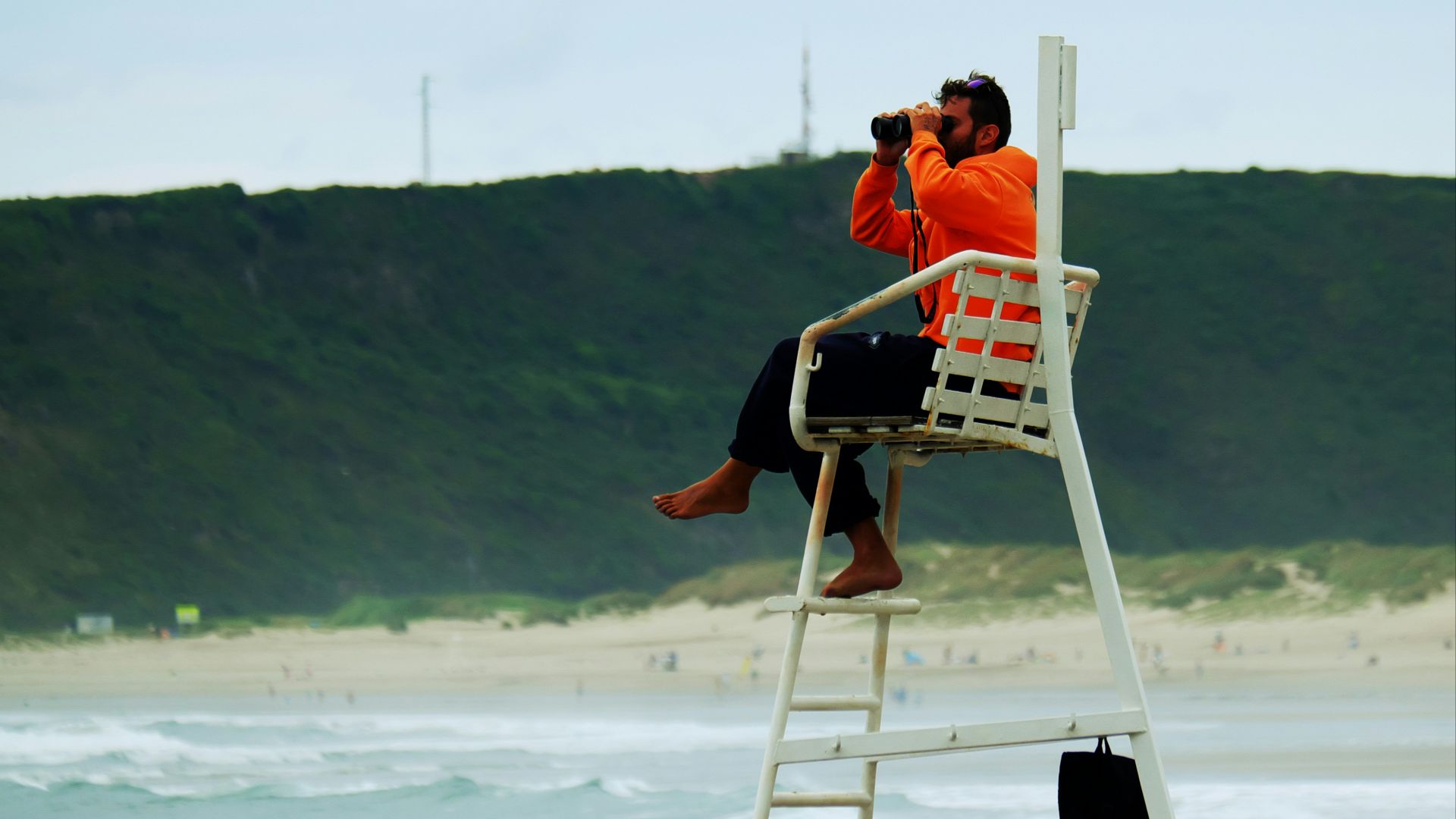 man in orange shirt sitting on white wooden folding chair on beach during daytime