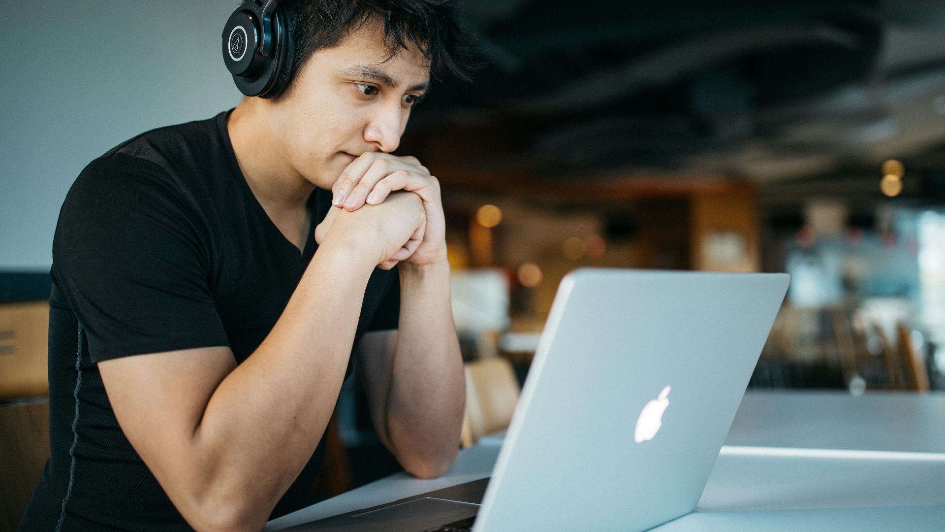 man wearing headphones while sitting on chair in front of MacBook
