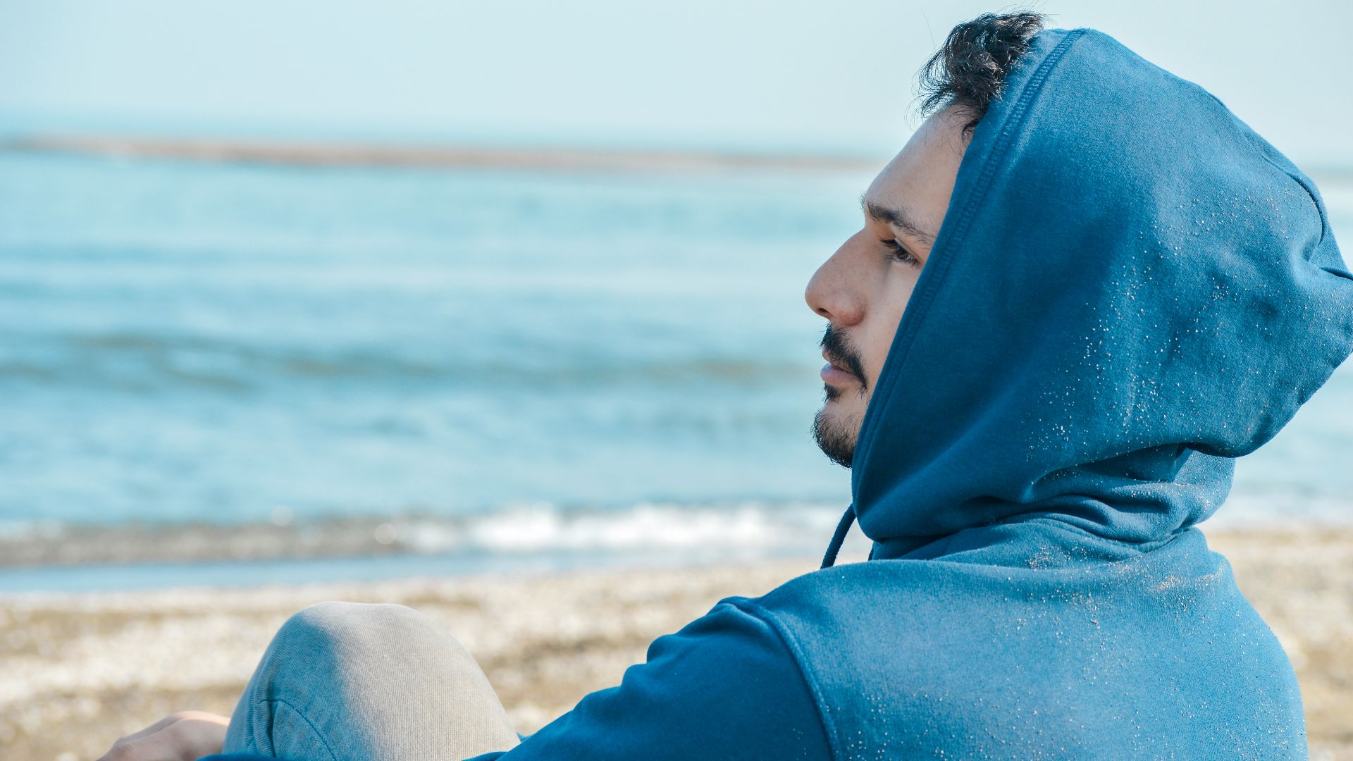 a man in a blue hoodie sitting on a beach