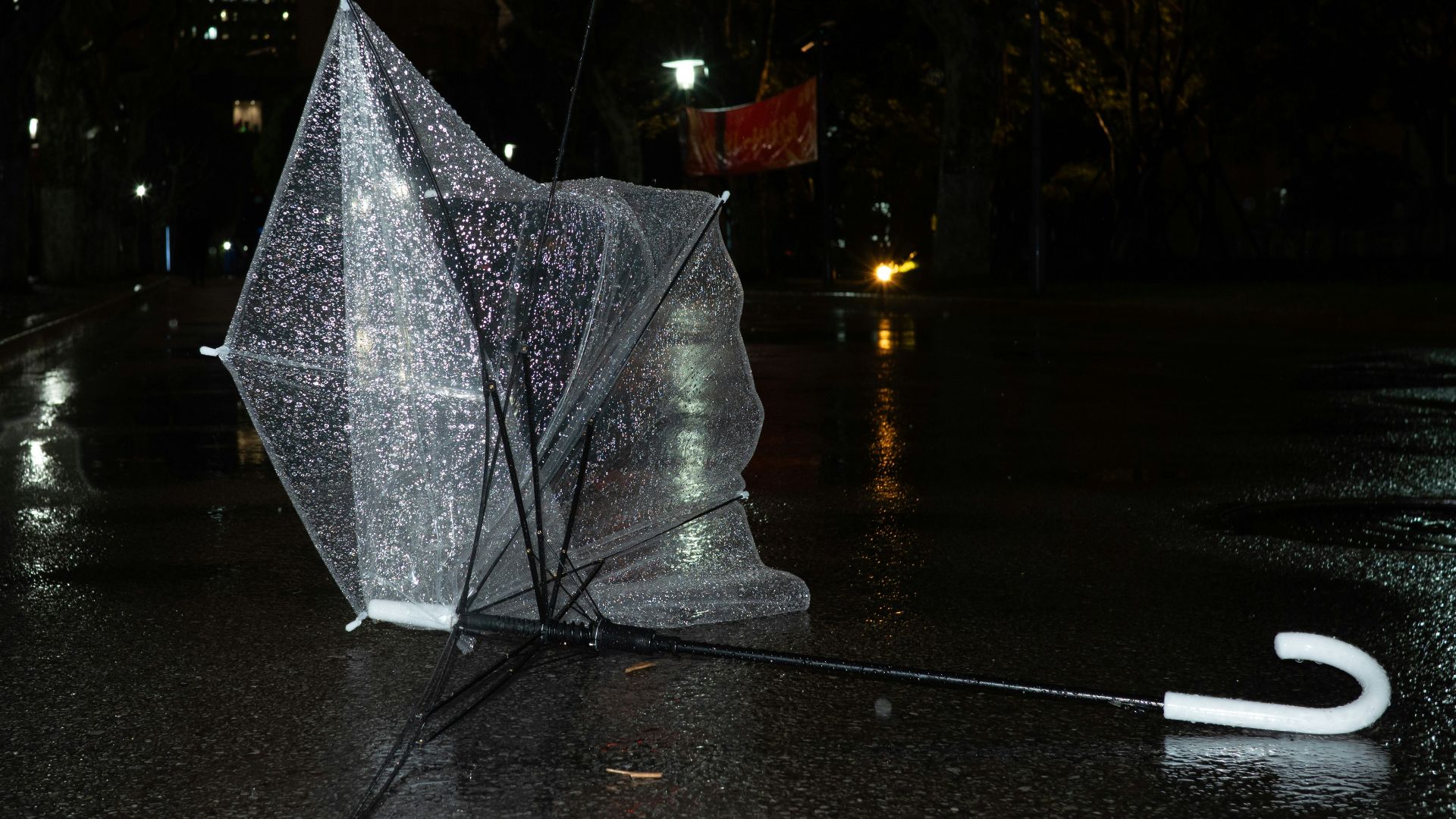 A broken umbrella lies on a wet street at night.