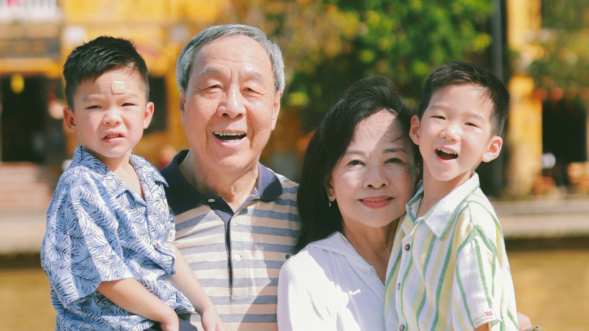 Grandparents holding smiling grandchildren outdoors.
