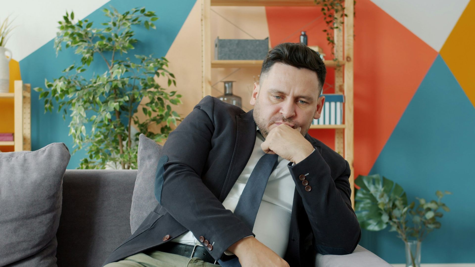 Man in suit sitting on couch looking thoughtful.
