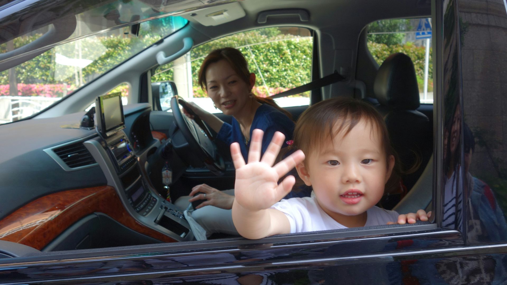 Child waves from car window with mother driving