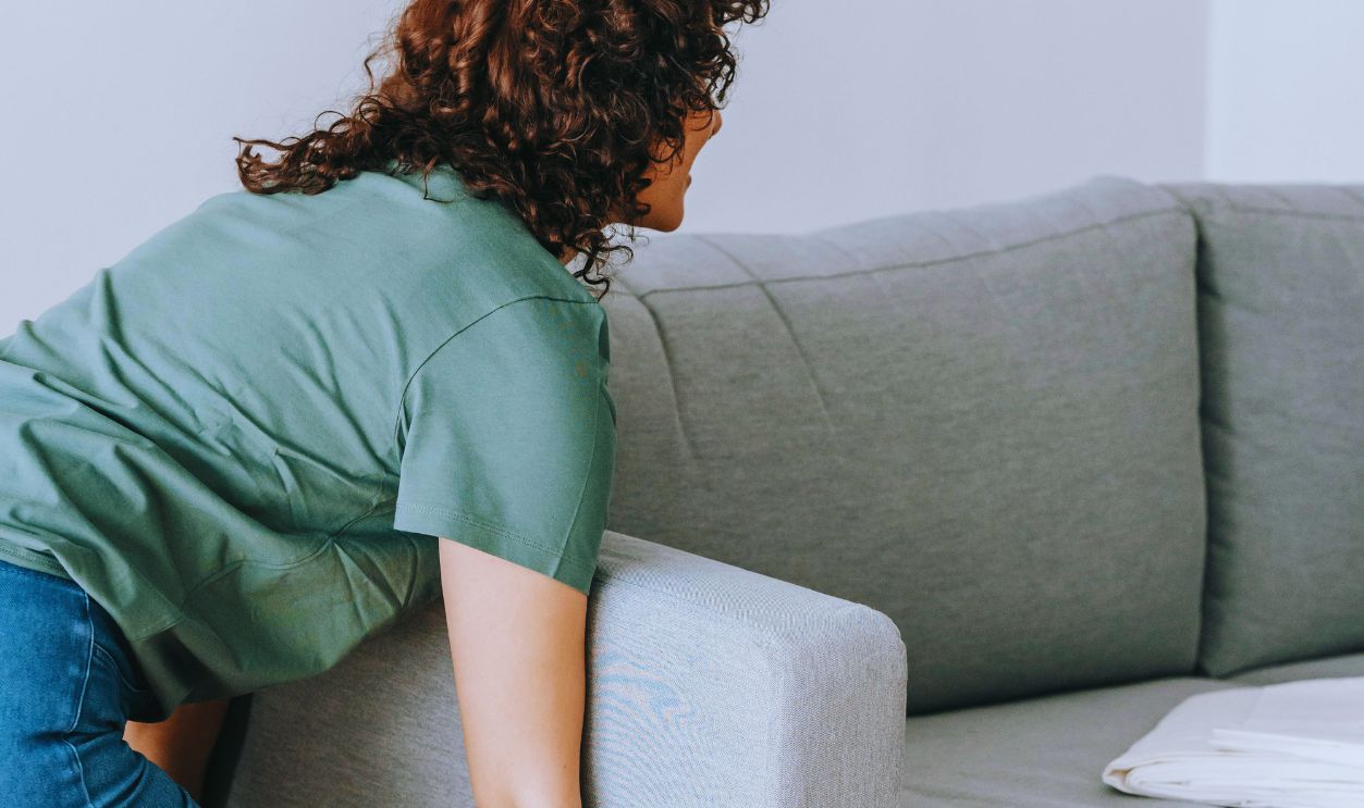 Woman in Green Shirt and Blue Denim Jeans Lifting A Gray Couch