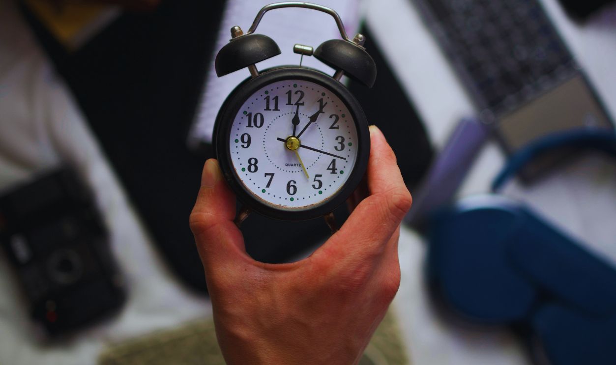 Hand Holding Alarm Clock Over Desk Setup