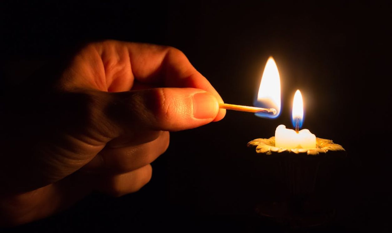 Person Holding Match Stick With Fire in Front of Candle With Fire