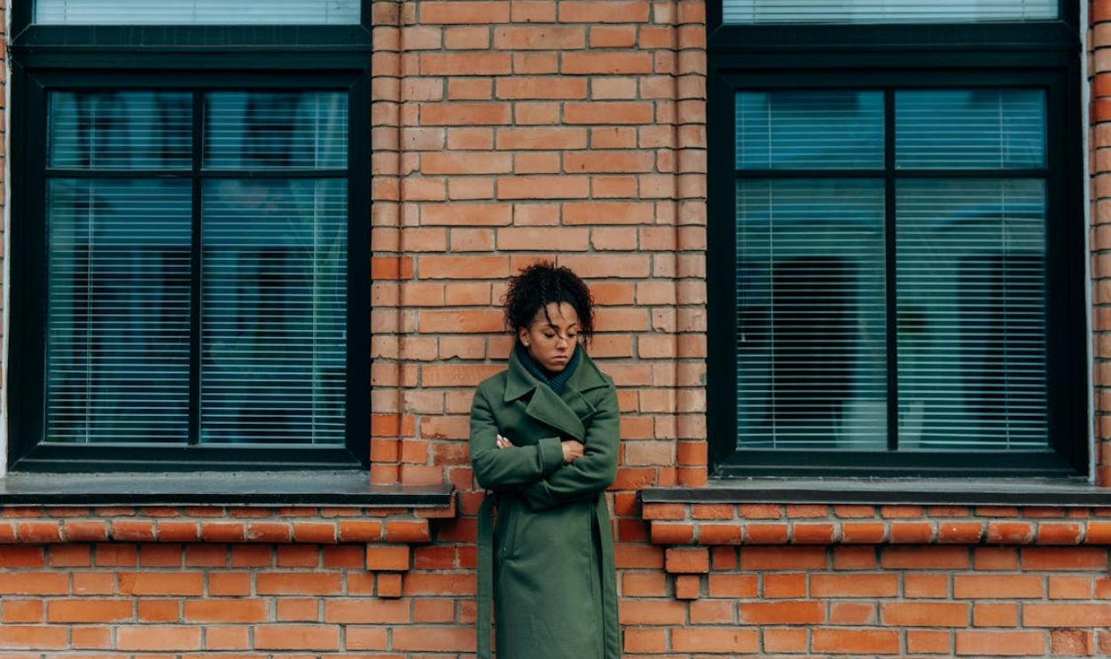Woman in Green Coat Leaning on a Brick Wall