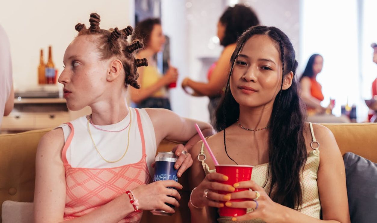 oman in Pink Sleeveless Dress Sitting Beside Woman in Gold Tank Top