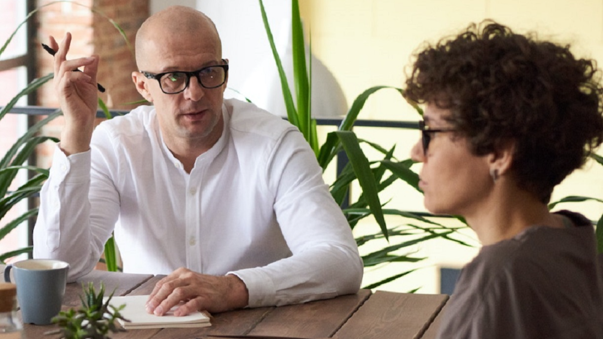 Man is having a office meeting with young female with short hair wearing dark shirt.