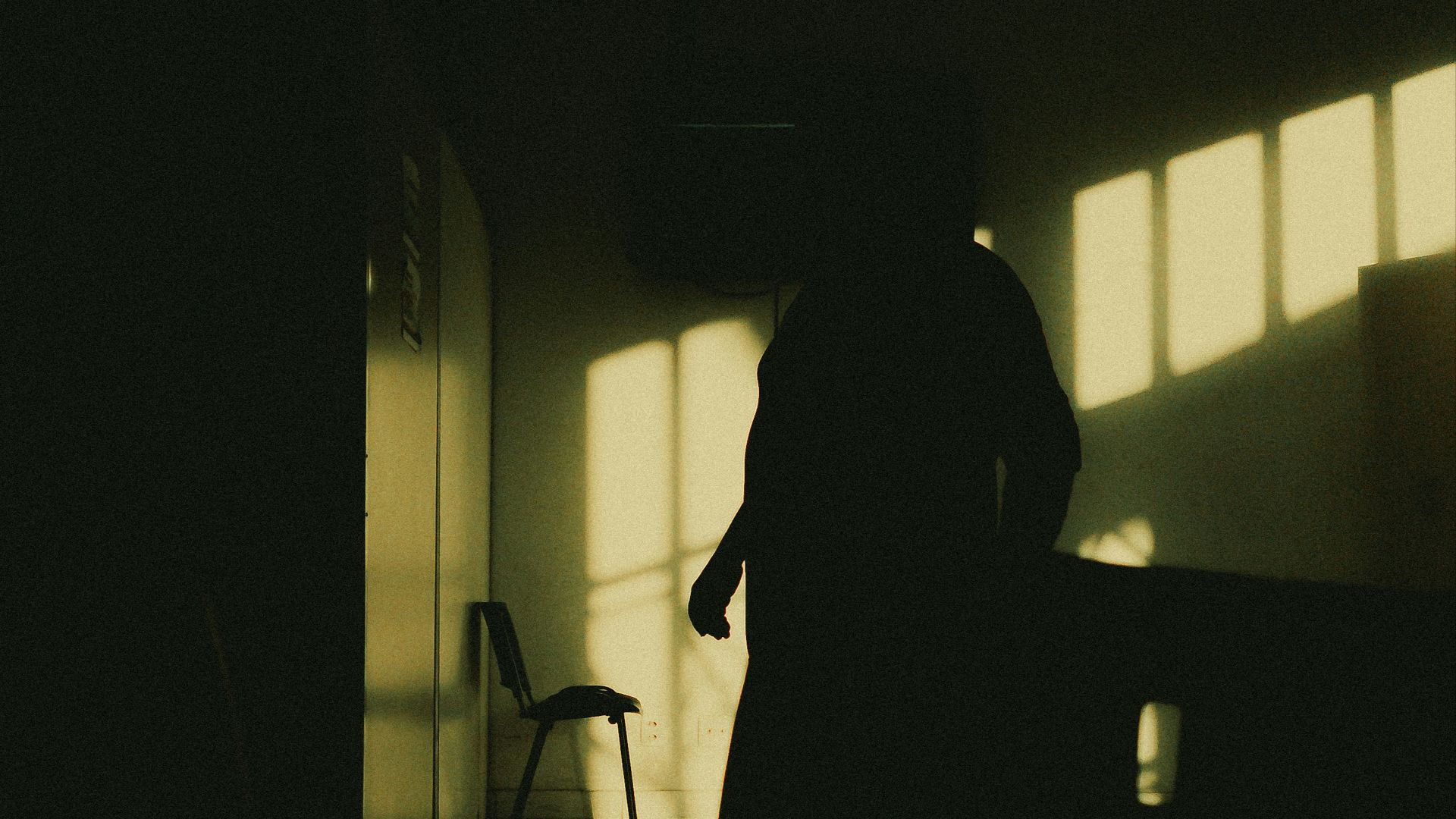 A dark figure stands in a dim room.