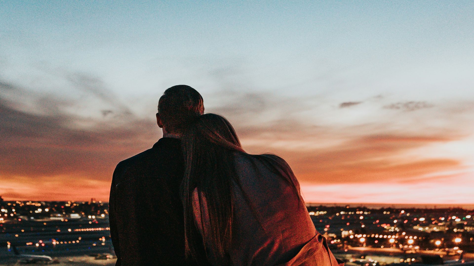 couple sitting on the field facing the city