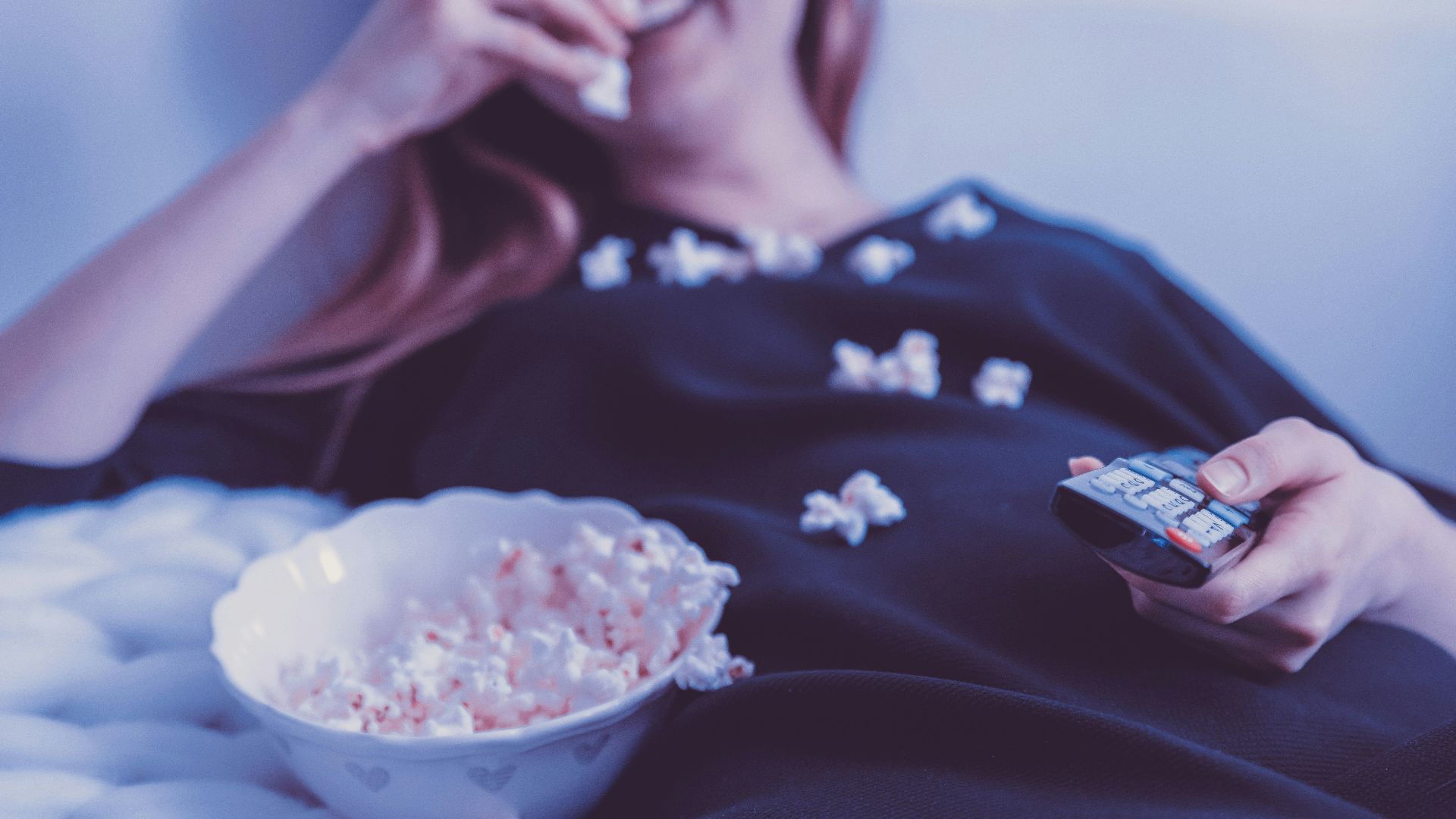 woman lying on bed while eating puff corn