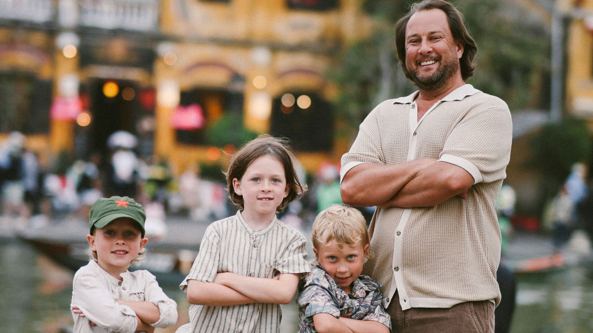 Father and three sons pose in front of yellow buildings.
